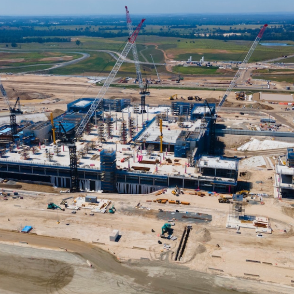 Aerial view of a large industrial construction site with multiple cranes and buildings under construction.