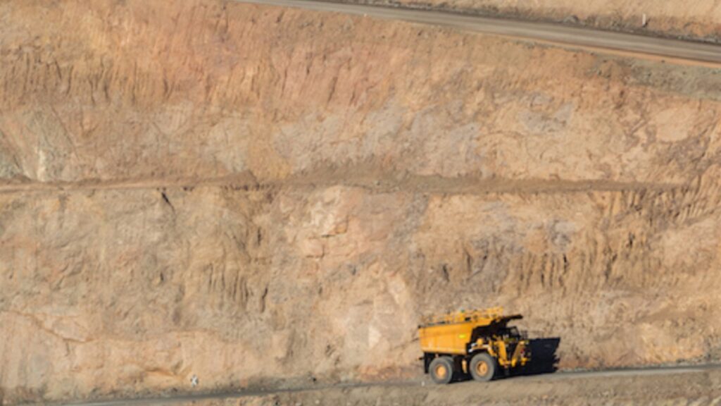 A haul truck on a haul road in a large open-pit mine, with terraced rock walls rising behind it.
