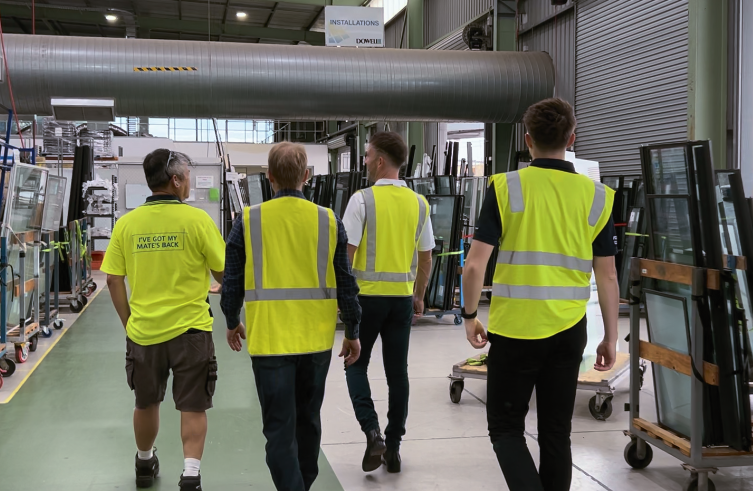 Four people in hi-vis walking through an aluminium and glass fabrication facility.