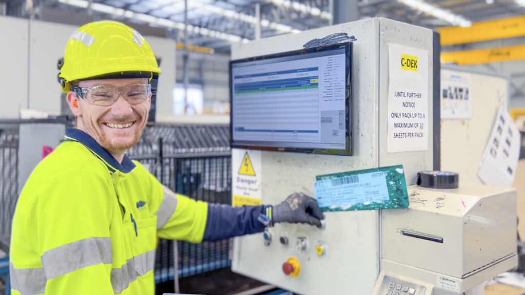 A smiling worker in hi-vis operating a machine control terminal in a steel factory.