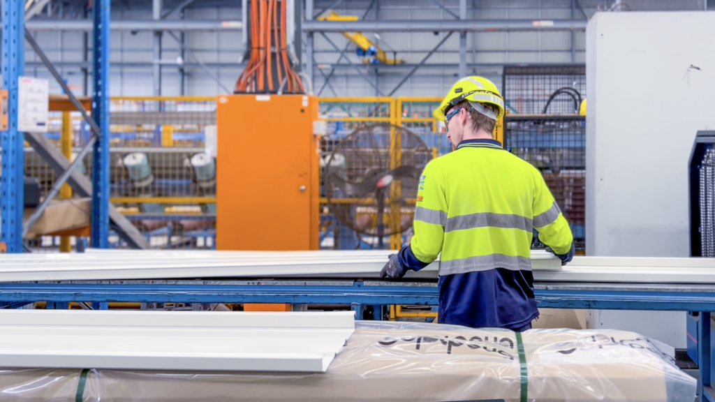A worker in hi-vis at a production line handling packaged steel products in a factory.