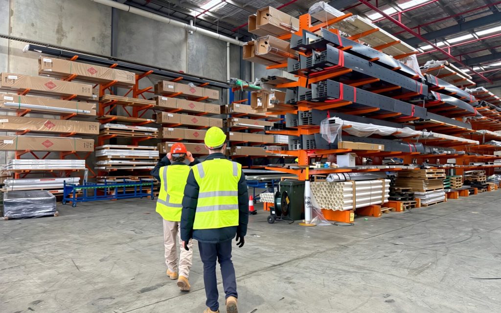 Workers walking past cantilever racking stacked with aluminium extrusions