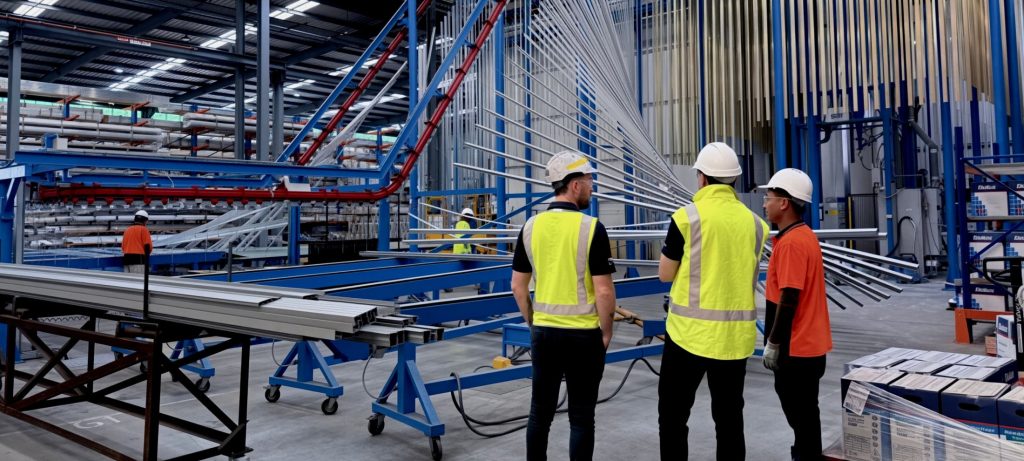 Workers in hi-vis and hard hats on an aluminium extrusion production line in a factory.
